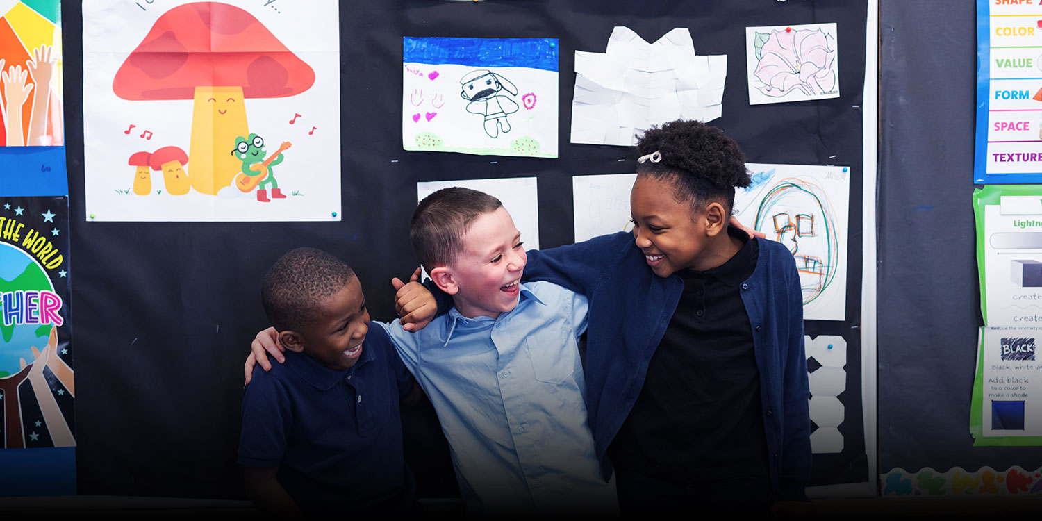 Smiling students with arm around each other in front of a bulletin board in a classroom.